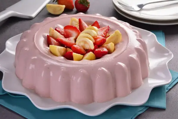 Deliciosa gelatina de fresa con trozos de fresa y guayaba fresca en el centro, servida en un plato blanco ondulado.