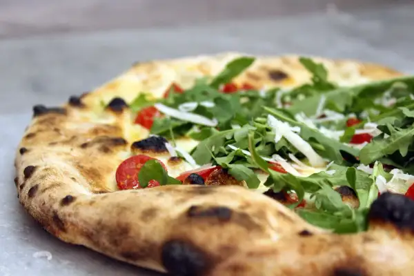 Zbliżenie na pizzę z rukolą, pomidorkami koktajlowymi i parmezanem.
