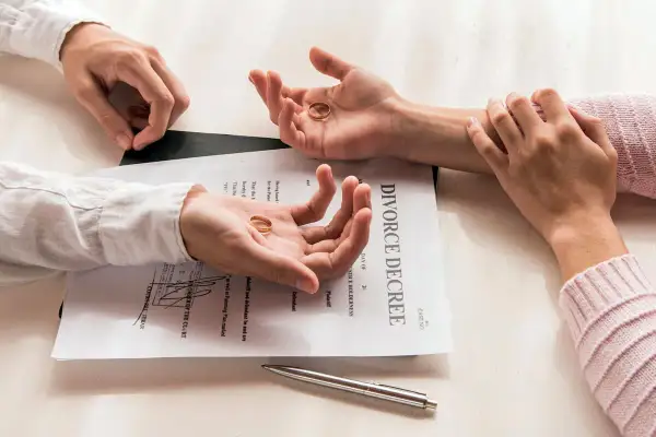 Dwie dłonie trzymają obrączki na tle dokumentu "DIVORCE DECREE". Czy do rozwodu potrzebny jest akt małżeństwa? Pytanie wisi w powietrzu.