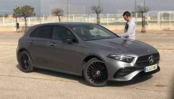Un hombre se apoya en un elegante Mercedes Clase A gris oscuro, listo para un viaje.