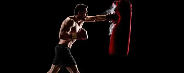 Boxer training to strengthen his chin for boxing, punching a red heavy bag with force.