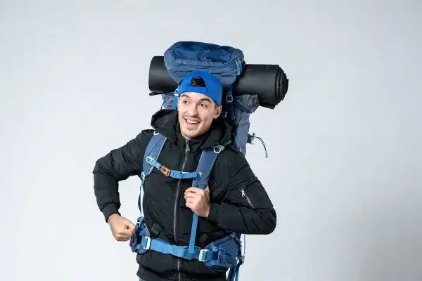 Un jeune homme souriant avec un grand sac à dos bleu, prêt pour l'aventure. On se demande : sac 70 litres combien de kilos ?