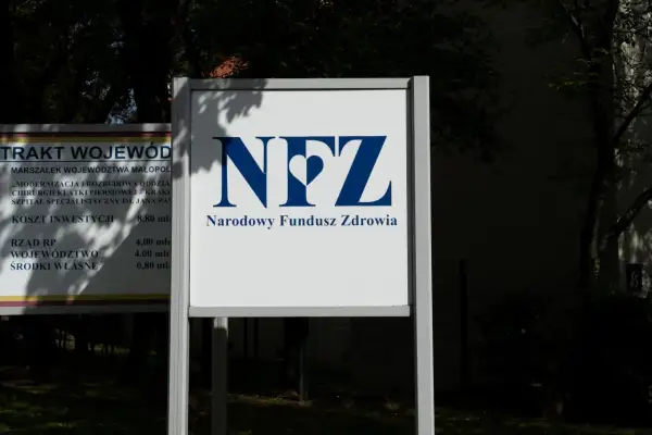 Tablica z logo NFZ i napisem Narodowy Fundusz Zdrowia. Obok tablica z informacjami o inwestycjach, jak sprawdzić oddział NFZ.