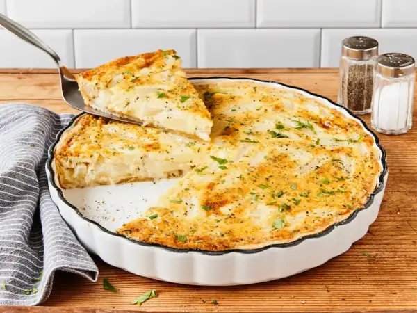 Eine köstliche Spargel Quiche wird serviert. Ein Stück wird mit einem Tortenheber herausgehoben, garniert mit frischer Petersilie.