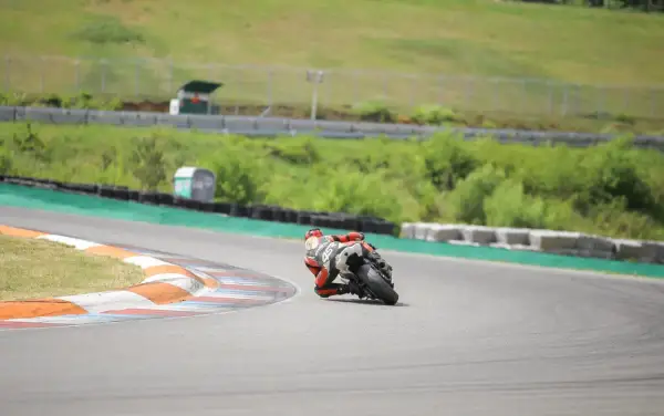 Motocyklista w czerwonym kombinezonie pochylony na zakręcie toru wyścigowego.