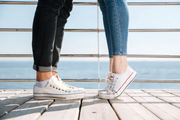 Para na drewnianym pomoście, w białych trampkach i jeansach. Idealne converse stylizacje damskie na letni dzień nad morzem.