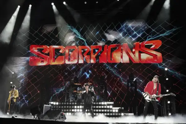 Zespół Scorpions na scenie z dużym logo zespołu i efektami świetlnymi.
