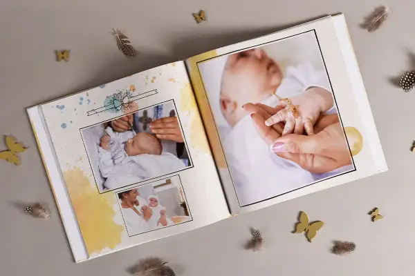Otwarta księga pamiątkowa z fotografiami niemowlęcia, ozdobiona piórkami i motylkami.