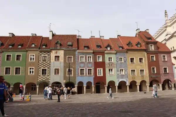 Kolorowe kamieniczki na Starym Rynku w Poznaniu, wspaniałe poznańskie atrakcje. Ludzie spacerują po brukowanym placu.
