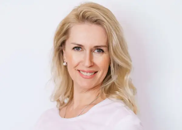 Uśmiechnięta blondynka po czterdziestce z fryzurą dodającą objętości cienkim włosom.