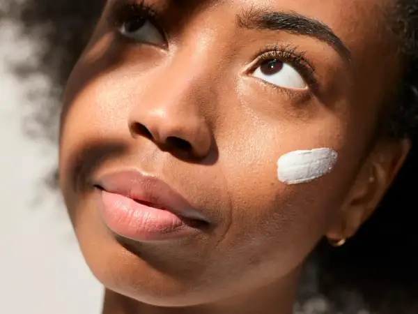 Geste doux pour mettre de la crème sur la joue d'une jeune femme, illuminée par la lumière du soleil.