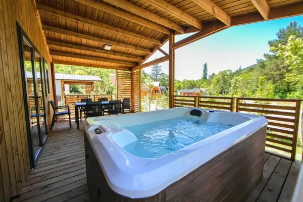 Terrasse en bois avec jacuzzi et table à manger, vue sur la nature. Idéal pour un séjour détente au camping de la ferme.
