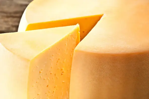 Kawałek sera Gouda z widocznymi oczkami i fragmentem całego kręgu sera.