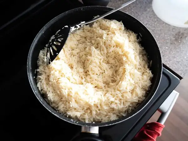 En stor kastrull med fluffigt, vitt ris står på spisen. En svart slev rör om i det nykokta riset, redo att serveras. Perfekt för en snabb middag, detta ris i kylen är en räddare i nöden.