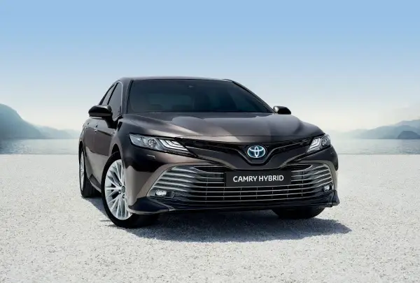Elegancka, ciemnobrązowa Toyota Camry Hybrid 2020 zaparkowana nad jeziorem, gotowa na podróż.