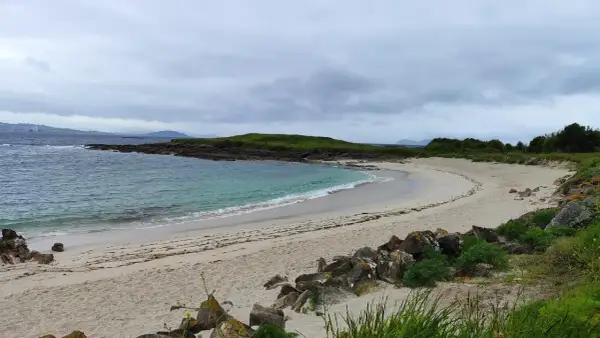 La serena playa Santa Marta de Cangas, con sus aguas turquesas y arena dorada, invita a la calma bajo un cielo nublado.