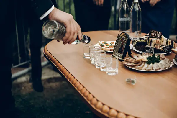 Na weselu nalewana jest wódka do kieliszków. Obok stoją zakąski i tort. Ile wódki na wesele?