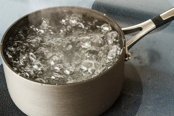Une casserole en métal sur une plaque de cuisson, l'eau est en train de bouillir avec des bulles et de la vapeur.