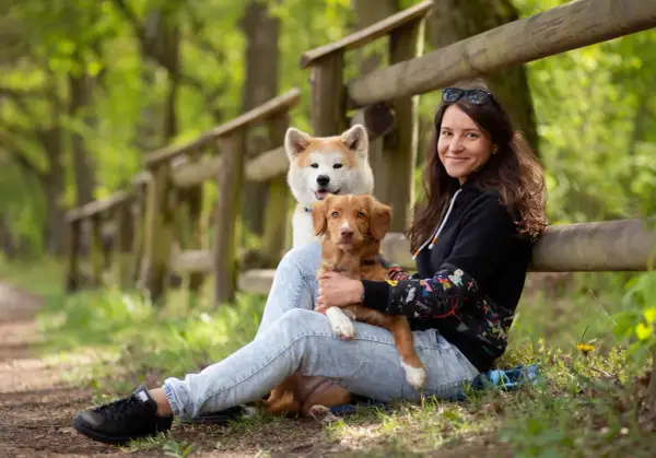 Kobieta z dwoma psami w lesie. Jeden piesek jest na jej kolanach, drugi za nim. Wskazówki, jak uspokoić sukę podczas cieczki, mogą być pomocne.