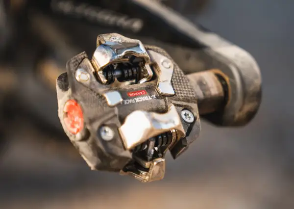 Close-up van een vuil racefiets pedaal met een carbon X-Track Race kliksysteem, klaar voor de volgende rit.