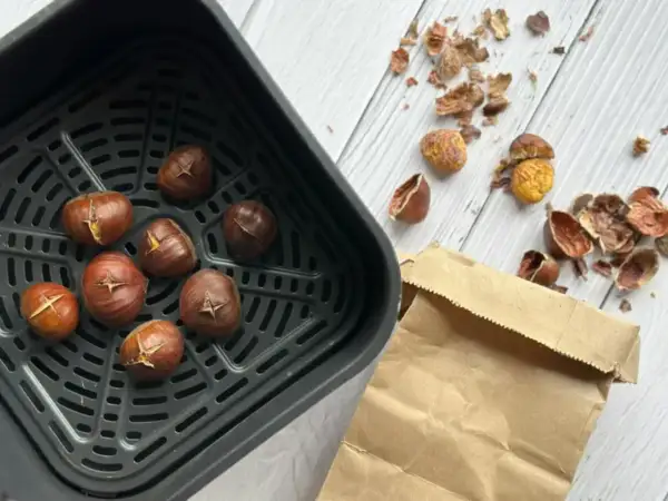 Châtaignes grillées dans un air fryer, prêtes à être dégustées. Les peaux éparpillées témoignent de leur préparation facile.