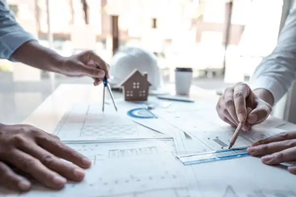 Architetti al lavoro su progetti edilizi, tra cui quelli che rientrano nella CILA. Si vedono mani che usano compasso, matita e righello sui disegni.