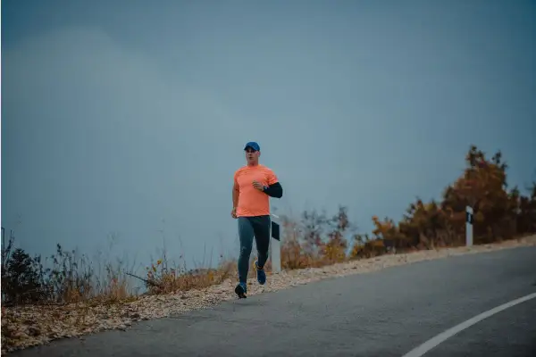 Mężczyzna w pomarańczowej koszulce i czapce biega po pustej drodze. Czy można biegać na czczo? To pytanie zadaje sobie wielu sportowców.