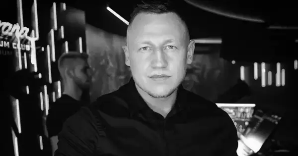 DJ Iroon w czerni, gotowy do rozkręcenia imprezy. W tle neonowe światła klubu.