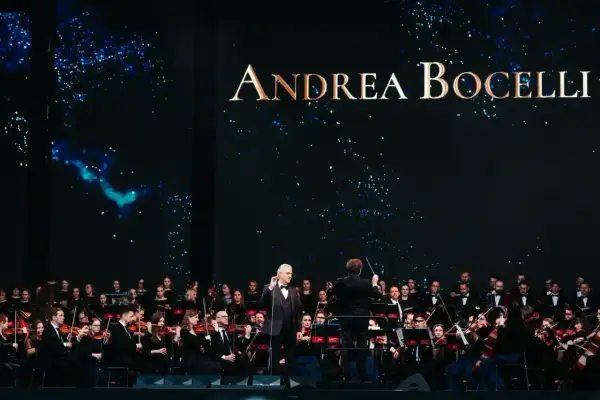 Andrea Bocelli koncert 2026. Wokalista śpiewa z orkiestrą symfoniczną na tle gwieździstego nieba.