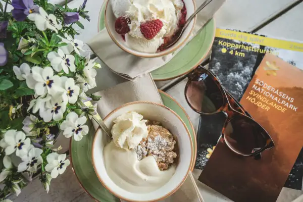 Fika med glass och smulpaj, perfekt för ett resmål i juni. Blommor och karta över Söderåsens nationalpark.