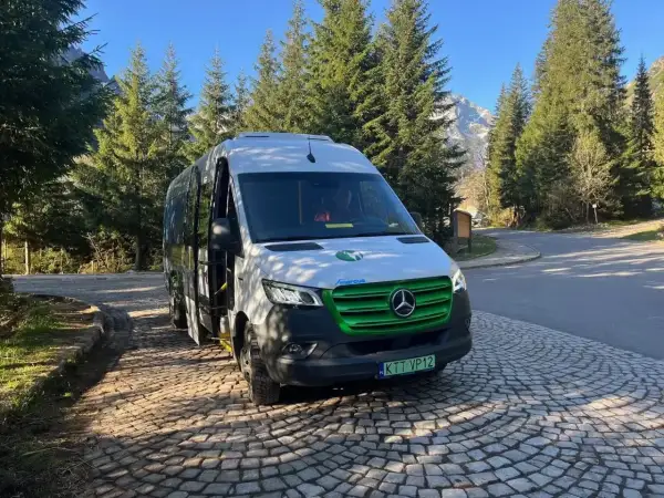Nowy, ekologiczny bus na Morskie Oko czeka na turystów. W tle góry i las.