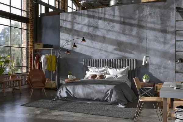 Przytulny soft loft z łóżkiem, fotelem i biurkiem. Duże okna wpuszczają światło, podkreślając surowy charakter wnętrza.