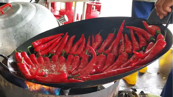 Viele rote Chilis brutzeln in einer Pfanne über offenem Feuer. Wenn der Chili zu scharf ist, was tun? Vielleicht mehr Öl hinzufügen?