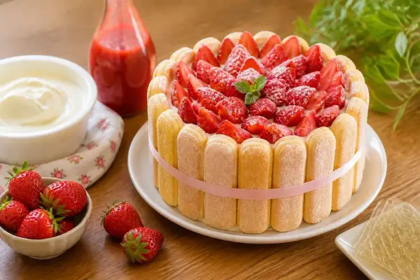 Délicieuse charlotte aux fraises, garnie de fruits rouges frais et entourée de biscuits à la cuillère. Un régal !