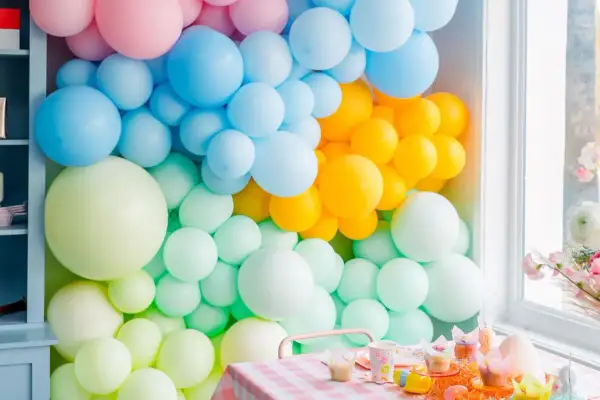 Kolorowa ściana z balonów: pastelowy róż, błękit, żółty i miętowy tworzą radosną oprawę dla świątecznego stołu.