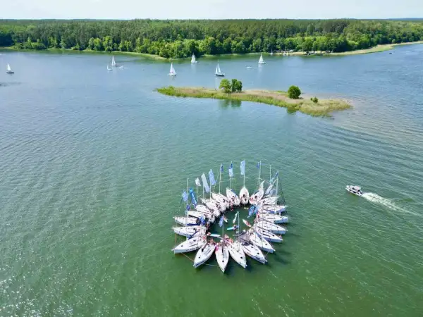 Żeglarska feta na Mazurach! Jachty tworzą krąg, a w tle las i jezioro. Idealne miejsce, by zapytać: gdzie na Mazury?