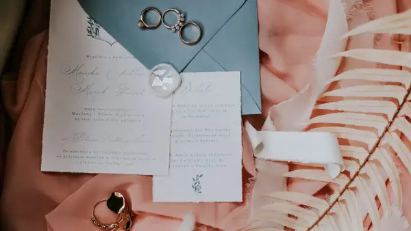 Eleganckie zaproszenie ślubne z obrączkami, pieczęcią i suszonymi liśćmi.