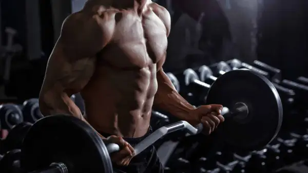 Uomo muscoloso in palestra esegue curl con bilanciere. Quante serie per gruppo muscolare sono necessarie per ottenere un fisico scolpito come questo?