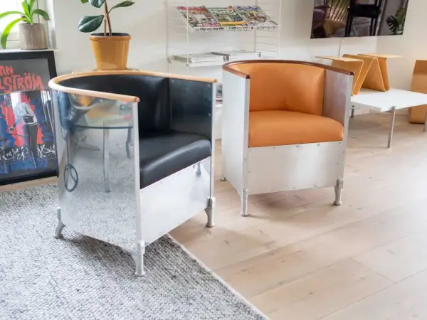 Två fåtöljer i källemo aluminium med svarta och orange lädersitsar. En spegelblank yta reflekterar rummet.