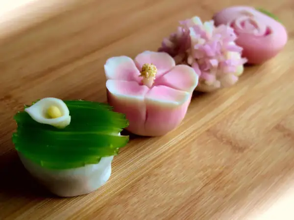 Délicates pâtisseries japonaises en forme de fleurs et de calla, aux couleurs pastel, sur fond de bois.