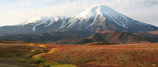 Majestätischer schneebedeckter Vulkan in einer weiten russischen Landschaft mit herbstlich gefärbten Hügeln im Vordergrund.