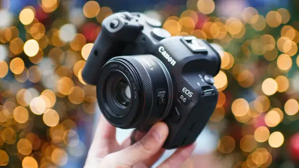Dłoń trzyma aparat Canon EOS R6 z obiektywem 50 mm f/1.8 STM na tle świątecznych światełek.