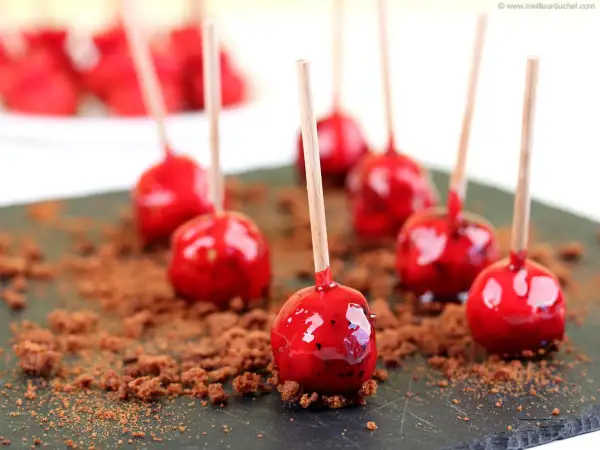 Sucettes de foie gras enrobées d'une fine couche rouge brillante, parsemées de miettes de pain d'épices sur une ardoise.
