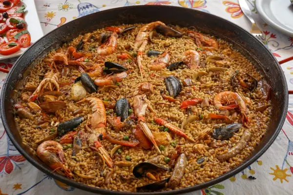 Une paella valenciana généreuse, débordant de riz, crevettes, moules et langoustines, prête à être dégustée.