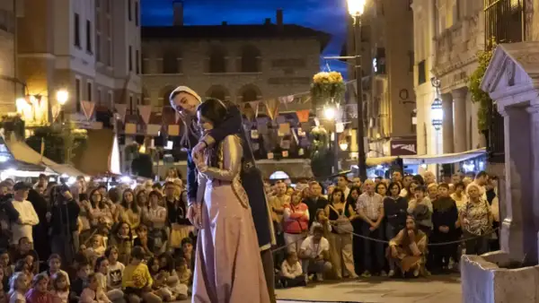 Una pareja se abraza en una calle iluminada por farolas, ante una multitud que observa. Podría ser la escena de "la partida de Diego".