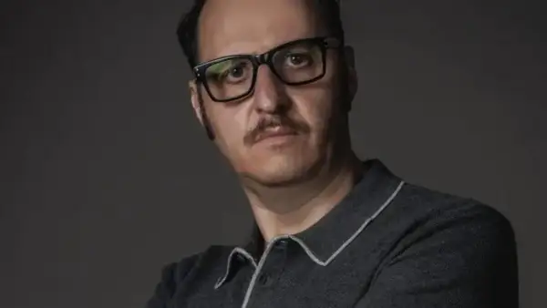Ritratto di Fausto Russo Alesi con occhiali neri e baffi, indossa una polo grigia.