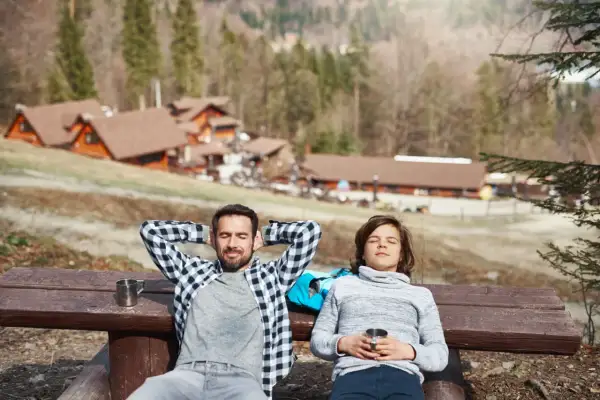 Un padre e un figlio si rilassano su una panchina in montagna, godendosi il sole dopo una passeggiata. Un perfetto weekend in montagna.