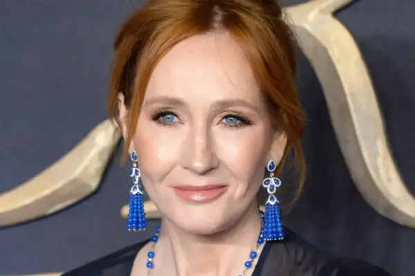 J.K. Rowling, która stworzyła postać Harry'ego Pottera, z niebieskimi oczami i rudymi włosami, w eleganckich, niebieskich kolczykach.
