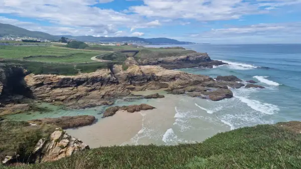 Senderistas disfrutan de las impresionantes rutas senderismo Foz, con acantilados rocosos, playas de arena y el mar azul.