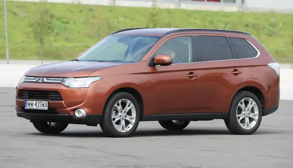 Brązowy Mitsubishi Outlander 3 na tle zielonego wzgórza.